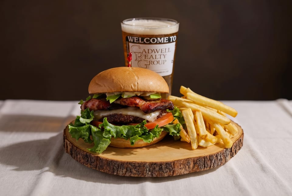 A burger with bacon, avocado, cheese, lettuce, and tomato, with fries and a beer.