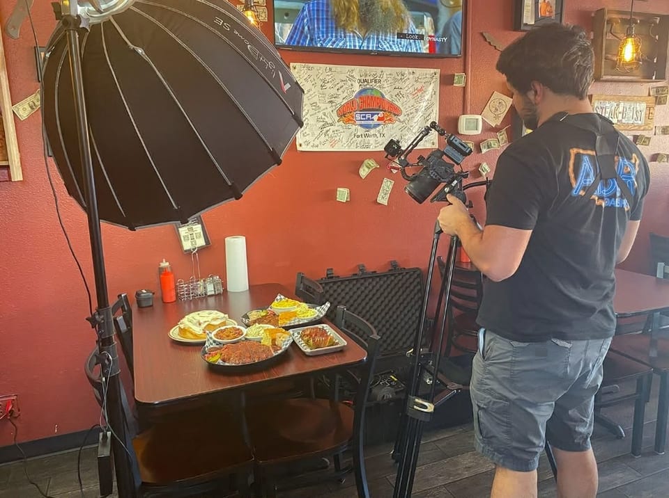 A person filming various dishes on a table with professional lighting in a restaurant.